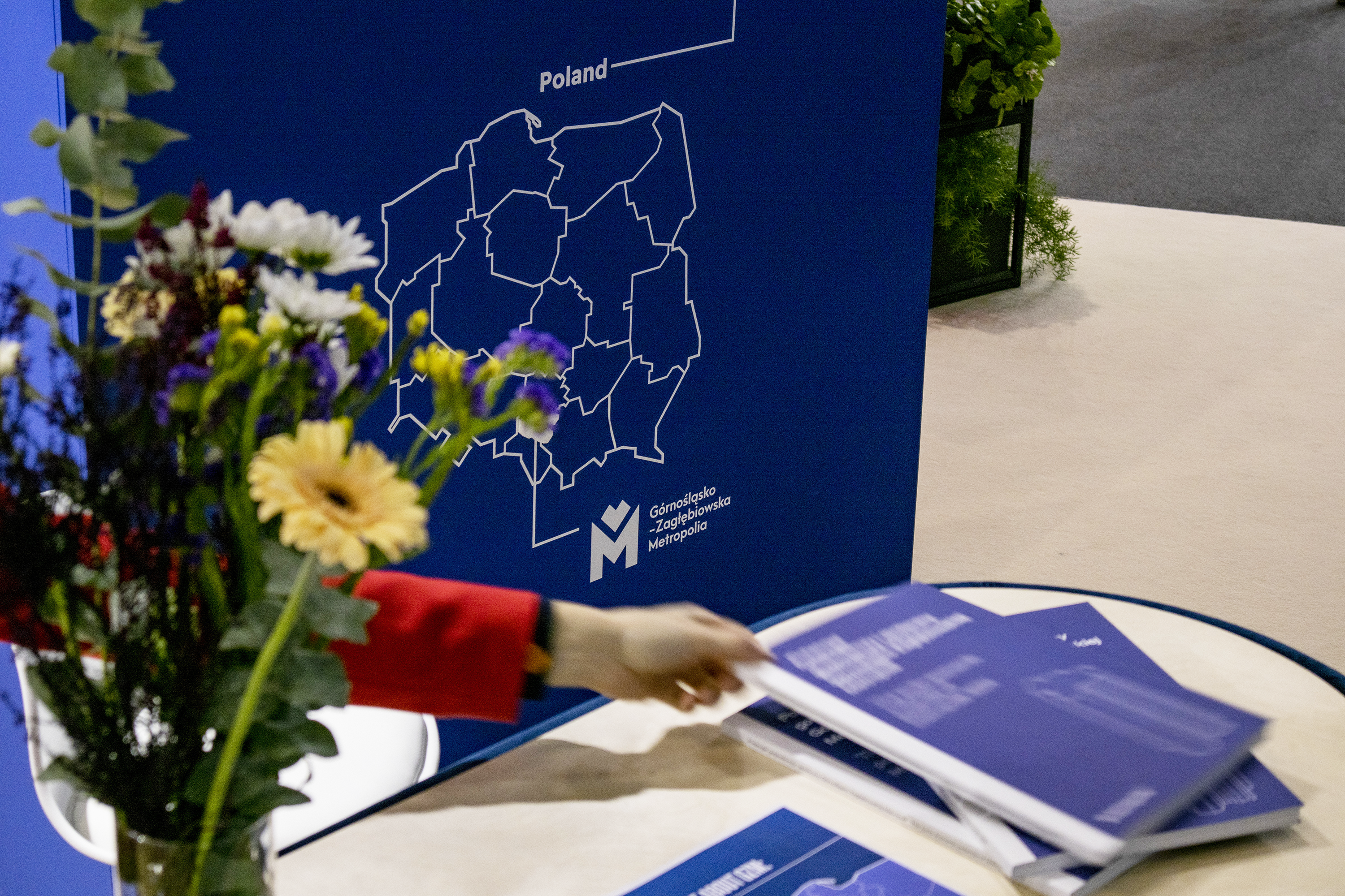 Close-up on the counter, a moving hand takes one of the catalogs, a bunch of flowers to the side.