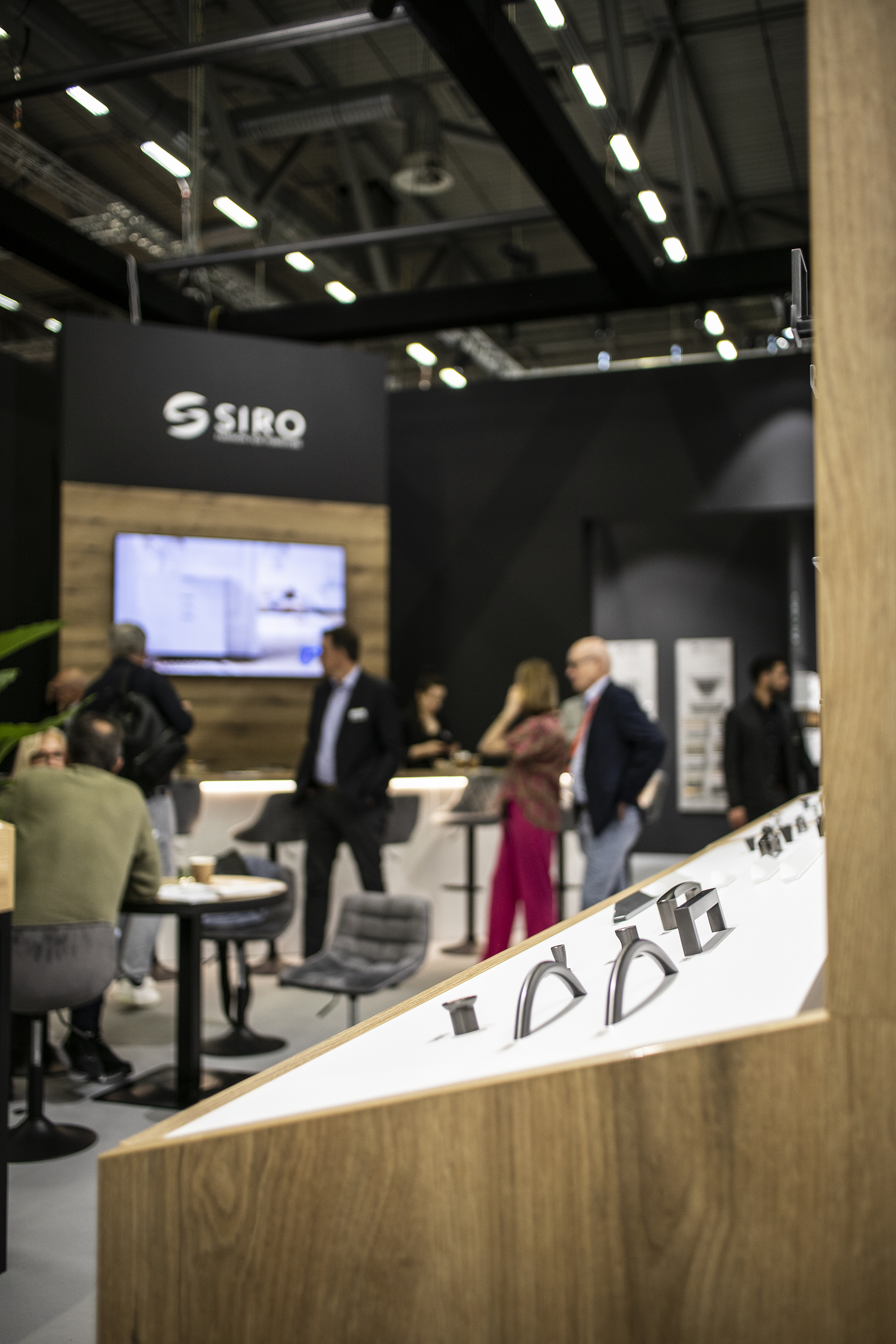 View of the interior of the stand, focus on the display, in the background people talking at the semi-circular counter and a wall with a TV set.